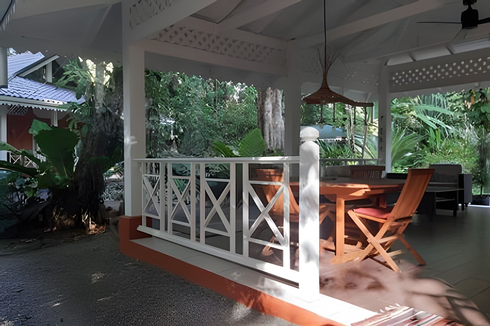 A covered outdoor seating area with a white railing, a table, and chairs.