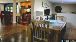 A dining area with wooden chairs and a table, a kitchen in the background, and a wall-mounted clock. - Relax & Explore – Sarasota Beaches & Downtown! (Sarasota)