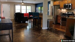 A spacious living area with a red sofa, a blue chair, and a dining table. The kitchen features wooden cabinets, a stainless steel refrigerator, and a microwave. - Relax & Explore – Sarasota Beaches & Downtown! (Sarasota)