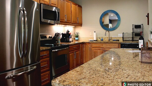 A kitchen with wooden cabinets, stainless steel appliances, granite countertops, and a round mirror on the wall. - Relax & Explore – Sarasota Beaches & Downtown! (Sarasota)