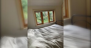 Een kamer met een enkel bed, een raam met uitzicht op groen en een metalen hoofdbord.