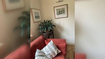 A room with a red sofa, a potted plant, and two framed pictures on the wall.