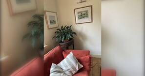 A room with a red sofa, a potted plant, and two framed pictures on the wall.