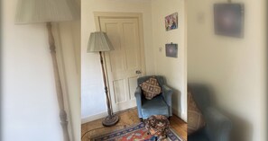 Een kamer met een blauwe fauteuil, een kamerbreed tapijt, een vloerlamp en een deur.