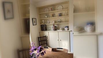 A dining area with a wooden table, a vase with purple flowers, and a cabinet with shelves of dishes.