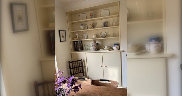 A dining area with a wooden table, a vase with purple flowers, and a cabinet with shelves of dishes.