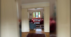 A hallway leading to a living room with a red sofa, a patterned rug, and a window with natural light.