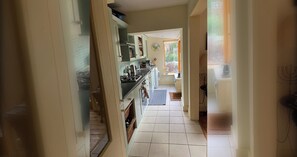 Een smalle gang die uitkomt in een keuken met een fornuis, oven en wasmachine.