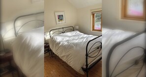 A bedroom with two beds, a wooden floor, a bedside table, a lamp, and a window.