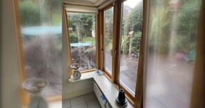 A room with a window overlooking a garden, a scale, and a kettle on the windowsill.