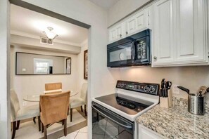 Cozinha compacta com armários brancos, micro-ondas, forno e bancada de granito.