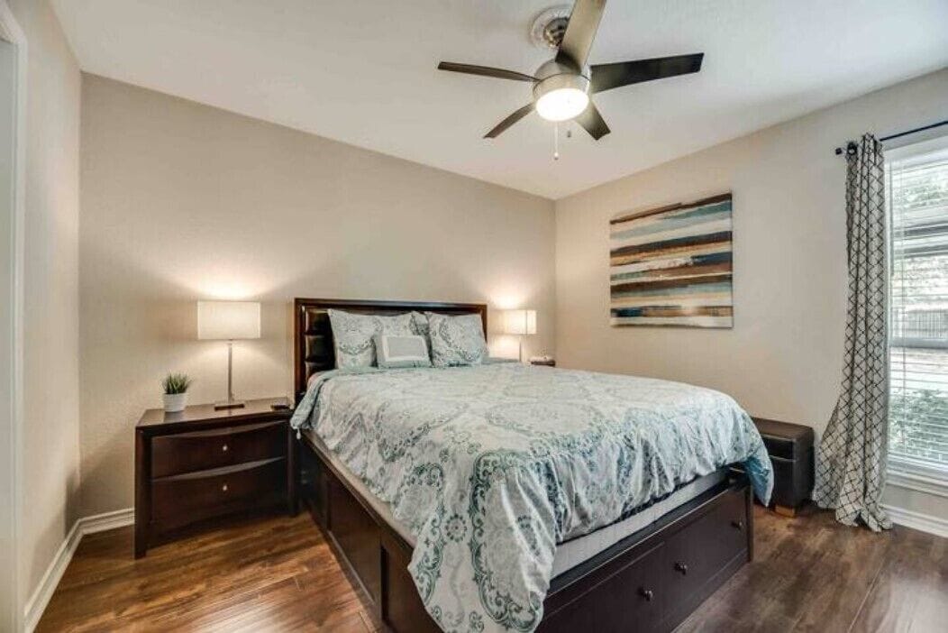 A bedroom with a bed, nightstands, a ceiling fan, and a window with curtains.
