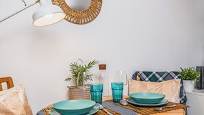Un'area pranzo con un tavolo rotondo in legno apparecchiato per due persone, con piatti e bicchieri color acquamarina, una bottiglia e una pianta.