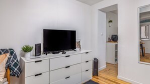Un soggiorno moderno con una TV a schermo piatto su un mobile bianco, una piccola pianta in vaso e un telecomando sul ripiano.
