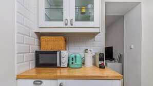 Una piccola cucina accessoriata con forno a microonde, tostapane, bollitore e un pensile con vetrine.