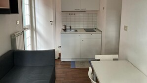 A compact kitchen with white cabinets, a sink, and a countertop. There is a door leading to another room and a small rug on the floor. - Casa giardino San Pietro (Roma)