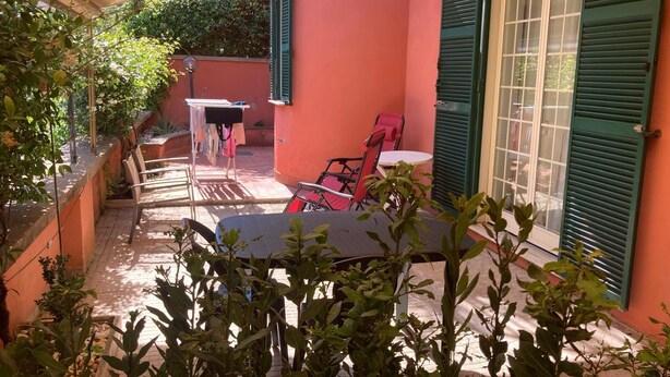 A covered patio with a table and chairs, a drying rack, and a view of a building with green shutters. - Casa giardino San Pietro (Roma)