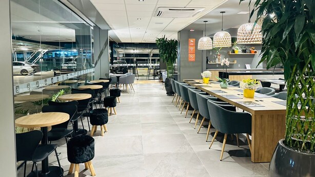 A modern restaurant with a long counter, black chairs, and potted plants. - Hotel 10 Sorriso (Sorriso)