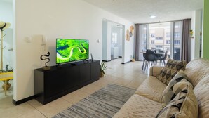 Un salon moderne doté d’un téléviseur à écran plat, d’un ventilateur de plafond et d’un coin repas avec une table et des chaises.