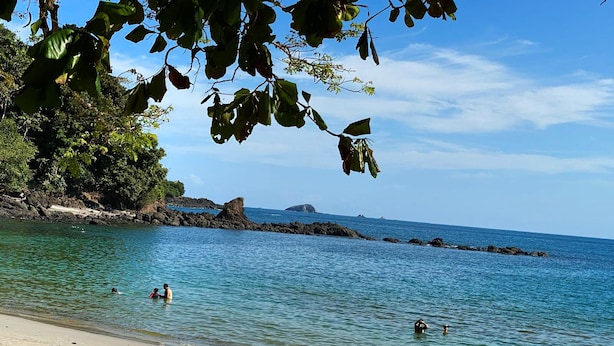 Une plage avec une eau turquoise et limpide, un rivage rocheux et des gens qui se baignent.