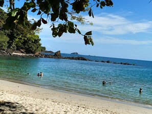 Une plage avec une eau turquoise et limpide, un rivage rocheux et des gens qui se baignent.