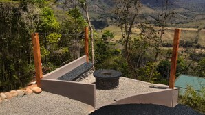 Un foyer en pierre, entouré d’un espace de détente en béton, offre une vue sur un paysage montagneux.