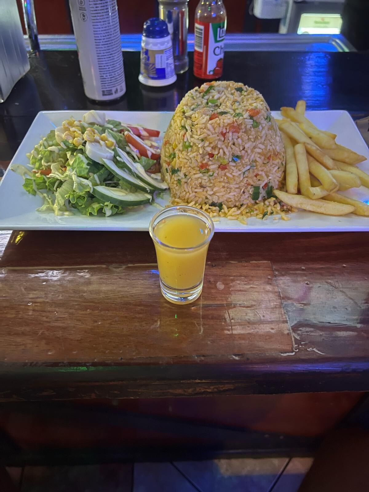 A plate of food with a salad, rice, and fries, and a glass of orange juice on a wooden table.
