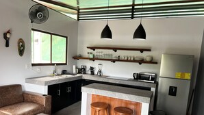 Une cuisine moderne dotée d’un îlot central, de tabourets en bois, d’un réfrigérateur et d’un coin repas avec une table et un canapé.