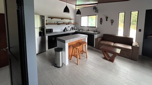 Une cuisine moderne dotée d’un îlot central, de tabourets de bar en bois et d’un coin salon avec un canapé en cuir marron.