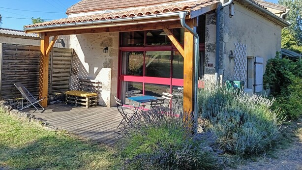 A rustic house with a tiled roof, a wooden deck, and a red-framed window. - Joli Gîte Rural Pour un Séjour à la Campagne (DIEULIVOL)