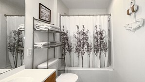 A bathroom with a toilet, a sink, a mirror, a shower curtain with a tree design, and a towel rack.