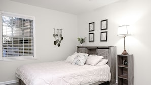 A bedroom with a bed, a bedside lamp, a wall-mounted plant, and framed pictures.