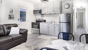 A modern kitchen with white cabinets, stainless steel appliances, and a black leather sofa.