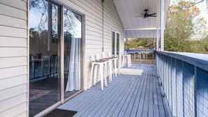 A covered outdoor area with a ceiling fan, a sliding glass door, and a row of white bar stools.