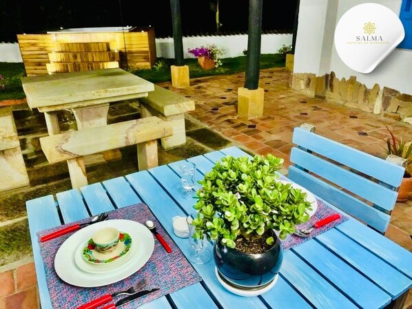 Un espacio de comedor al aire libre con una mesa dispuesta para dos, una planta en maceta y un banco.