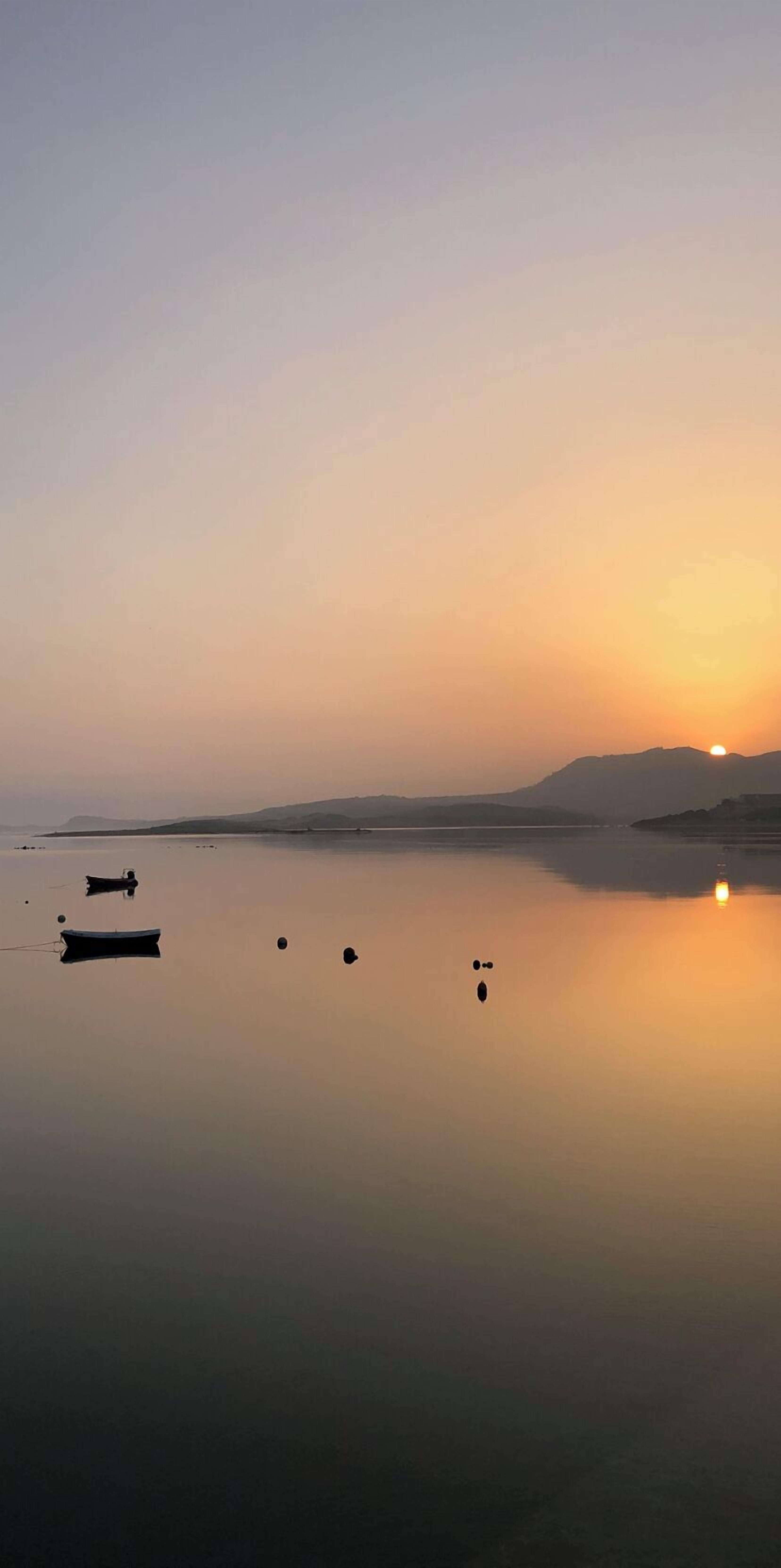 A calm lake at sunset with boats and buoys.