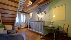 Una sala de estar acogedora con suelo de madera, un sofá azul, una silla de madera, un escritorio con un florero y una escalera con barandilla blanca.