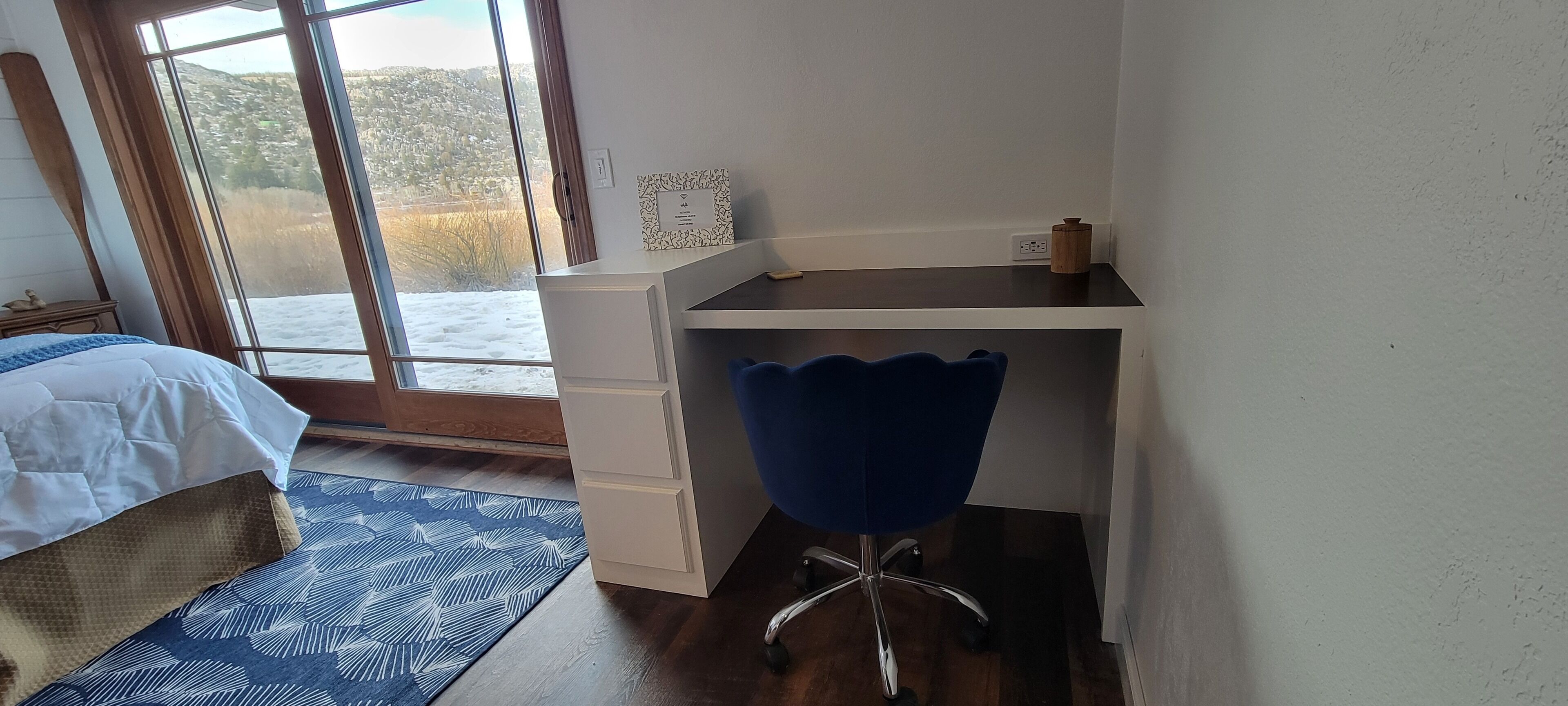 Quarto com cama, escrivaninha, cadeira e vista para uma paisagem nevada pela janela.