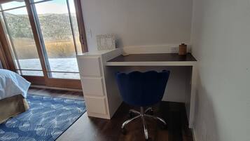 Quarto com cama, escrivaninha, cadeira e vista para uma paisagem nevada pela janela.