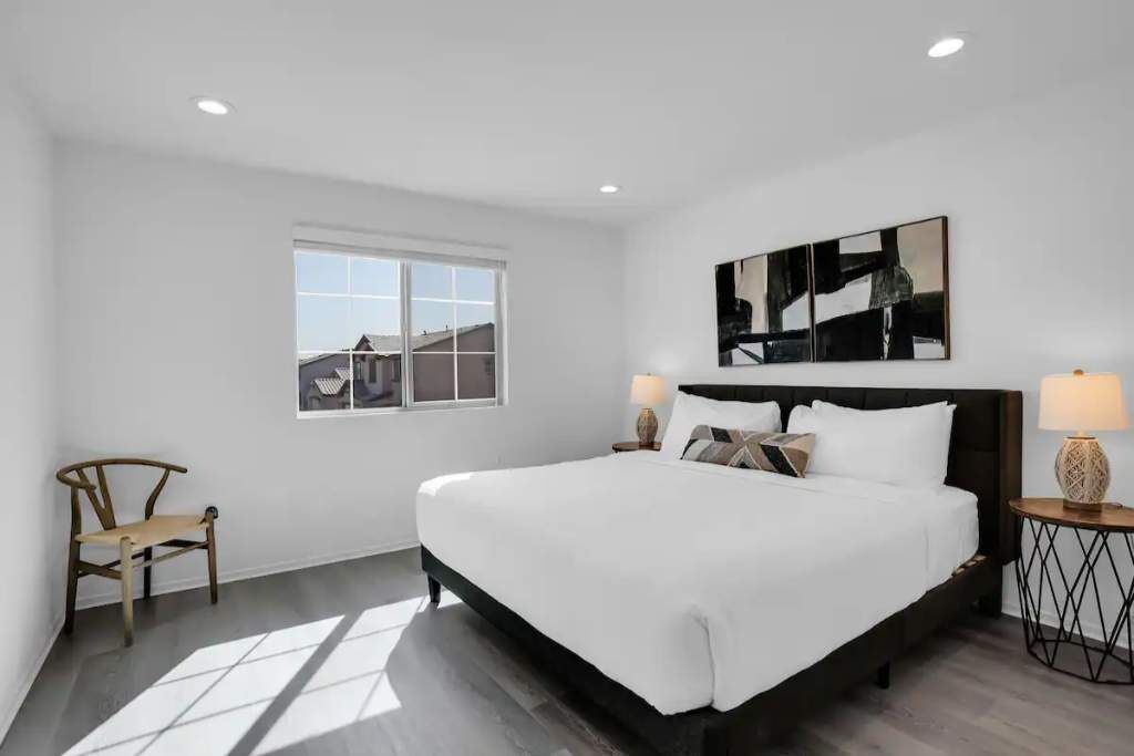 Une chambre moderne avec un grand lit, deux tables de chevet avec des lampes, une fenêtre donnant sur un beau paysage et une chaise en bois.