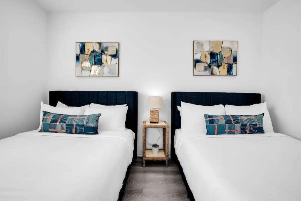 Ein Hotelzimmer mit zwei Betten, weißer Bettwäsche und abstrakter Kunst an den Wänden.