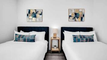 Ein Hotelzimmer mit zwei Betten, weißer Bettwäsche und abstrakter Kunst an den Wänden.