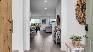 A modern interior with a wooden door, a dining area, and a living room with a sofa and a decorative wall piece. - The Chateau- Pool, Spa, BBQ, Fire pit, Sleeps 19 (Coachella)