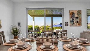 A dining area with a table set for four, including plates, bowls, and glasses, with a view of greenery outside. - The Chateau- Pool, Spa, BBQ, Fire pit, Sleeps 19 (Coachella)