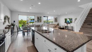 A modern kitchen with granite countertops, white cabinetry, and a large island. - The Chateau- Pool, Spa, BBQ, Fire pit, Sleeps 19 (Coachella)
