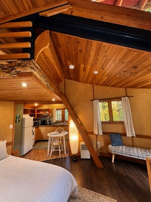 A cabin interior with a loft bedroom, a dining area, and a kitchen.