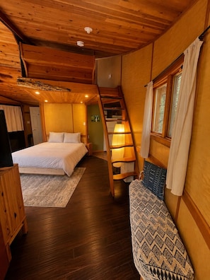A room with a bed, a sofa, a lamp, a staircase, and a window.