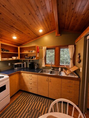 A compact kitchen with wooden cabinets, a microwave, a stove, and a sink.