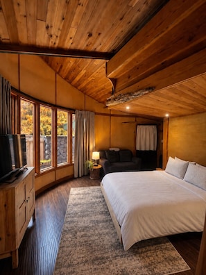 A bedroom with a wooden ceiling, a bed, a TV, and a window with curtains.