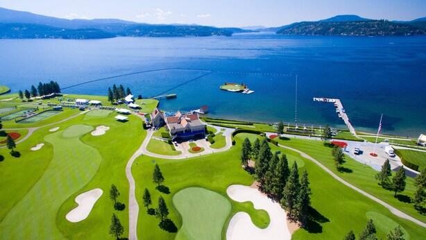 Vista aérea de un campo de golf con un club house, búnkeres de arena y un muelle que se adentra en un lago.